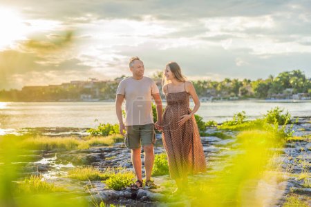 Photo for A happy, mature couple over 40, enjoying a leisurely walk on the waterfront On the Sunset, their joy evident as they embrace the journey of pregnancy later in life. - Royalty Free Image
