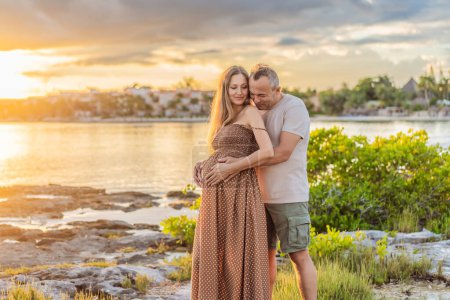 Photo for A happy, mature couple over 40, enjoying a leisurely walk on the waterfront On the Sunset, their joy evident as they embrace the journey of pregnancy later in life. - Royalty Free Image