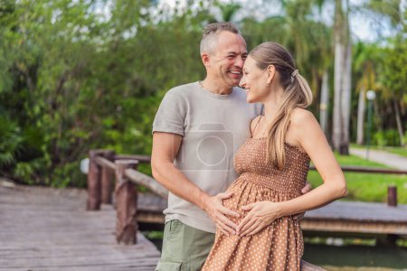 Foto de Una pareja feliz y madura de más de 40 años, disfrutando de un tranquilo paseo por un parque, su alegría evidente al abrazar el viaje del embarazo más adelante en la vida. - Imagen libre de derechos