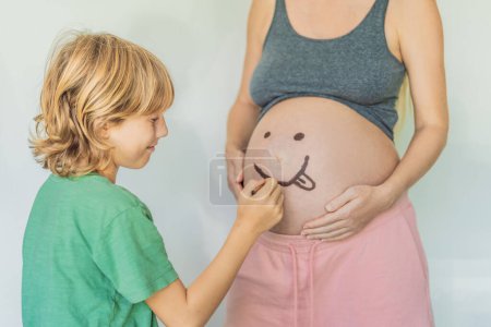 Photo for Adorable moment as a son adds a touch of joy to his mothers pregnancy, playfully drawing a funny face on her baby bump, creating cherished memories. - Royalty Free Image