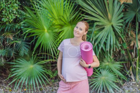 Foto de La mujer embarazada enérgica toma su entrenamiento al aire libre, usando una alfombra de ejercicio para una sesión de ejercicio al aire libre refrescante y consciente de la salud. - Imagen libre de derechos