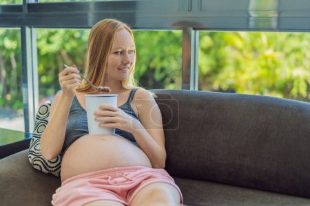 Glückliche schwangere junge Frau isst Eis.