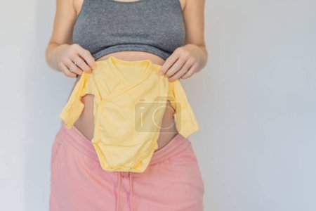 In a tender moment of anticipation, a pregnant woman cradles her unborn babys clothes in her hands, savoring the sweetness of preparing for the little ones arrival.