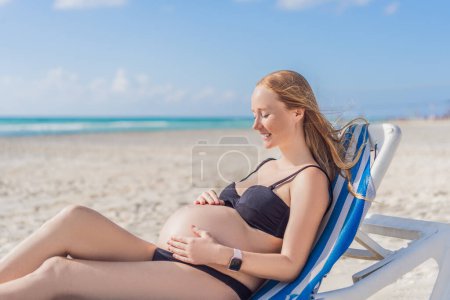 Téléchargez les photos : Se prélasser dans la tranquillité balnéaire, une femme enceinte se prélasse sur une chaise longue, embrassant l'ambiance apaisante de la plage pour un moment de détente sereine. - en image libre de droit