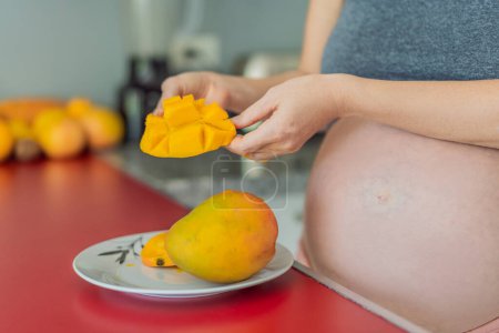 Téléchargez les photos : Une femme enceinte habile coupe délicatement en mangue mûre, savourant un moment de joie culinaire et nourrissant sa grossesse avec un régal frais et savoureux. - en image libre de droit