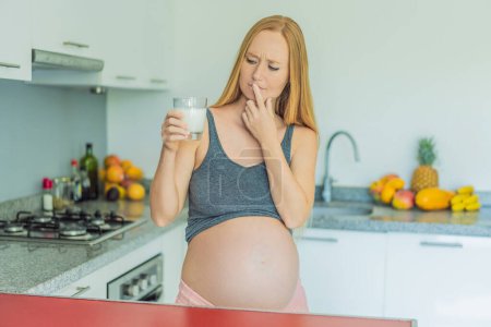 Weighing the pros and cons of milk during pregnancy, a thoughtful pregnant woman stands in the kitchen with a glass, contemplating the decision to include or avoid milk for her and her babys well