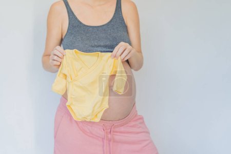 In a tender moment of anticipation, a pregnant woman cradles her unborn babys clothes in her hands, savoring the sweetness of preparing for the little ones arrival.