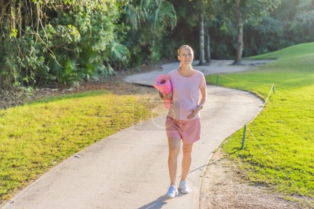La mujer embarazada enérgica toma su entrenamiento al aire libre, usando una alfombra de ejercicio para una sesión de ejercicio al aire libre refrescante y consciente de la salud.