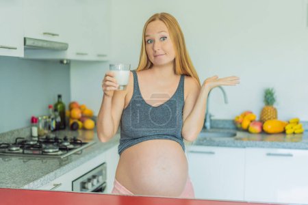 Beim Abwägen der Vor- und Nachteile von Milch während der Schwangerschaft steht eine nachdenkliche Schwangere mit einem Glas in der Küche und überlegt, ob sie und ihre Babys Milch gut aufnehmen oder vermeiden sollen.