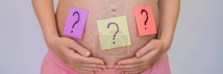 Téléchargez les photos : Choisir le nom du bébé. Femme enceinte confondue avec des points d'interrogation sur des autocollants en papier sur le ventre. BANNER, FORMAT LONG - en image libre de droit