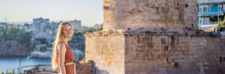 Touristin im Hintergrund des Hidirlik-Turms in Antalya vor dem Hintergrund der mediterranen Bucht des antiken Viertels Kaleici, Türkei. Türkiye. BANNER, LANG FORMAT