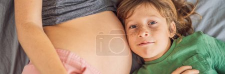 BANNER, LONG FORMAT Young beautiful pregnant woman and eldest son. The cute boy leaned his ear against his mothers belly. Expecting a baby in the family concept. Preparing an older child for a