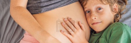 BANNER, LONG FORMAT Young beautiful pregnant woman and eldest son. The cute boy leaned his ear against his mothers belly. Expecting a baby in the family concept. Preparing an older child for a
