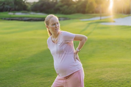 Mujer embarazada experimenta dolor de espalda al aire libre, buscando alivio y comodidad durante el embarazo con un suave estiramiento al aire libre o descanso.