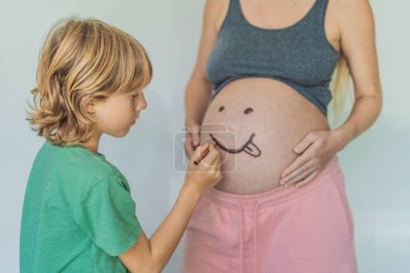 Adorable moment as a son adds a touch of joy to his mothers pregnancy, playfully drawing a funny face on her baby bump, creating cherished memories.
