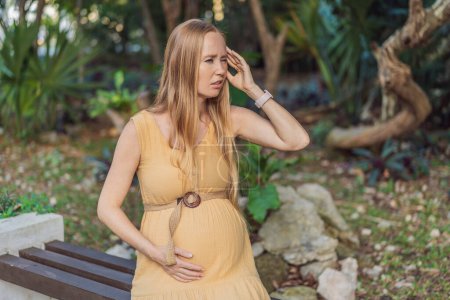 A pregnant woman experiences a moment of discomfort, grappling with a headache during pregnancy, highlighting the common challenge and the need for proper self-care and attention to maternal well