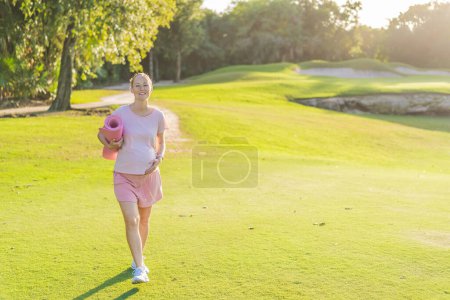 La mujer embarazada enérgica toma su entrenamiento al aire libre, usando una alfombra de ejercicio para una sesión de ejercicio al aire libre refrescante y consciente de la salud.