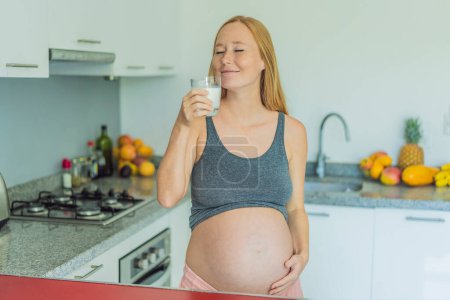 Pesant le pour et le contre du lait pendant la grossesse, une femme enceinte réfléchie se tient dans la cuisine avec un verre, envisageant la décision d'inclure ou d'éviter le lait pour elle et ses bébés bien