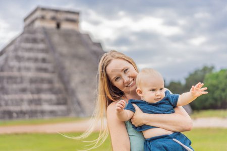 Hermosa turista y su hijo bebé observando la antigua pirámide y templo del castillo de la arquitectura maya conocido como Chichén Itzá. Estas son las ruinas de este antiguo precolombino
