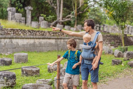 Padre y dos hijos turistas observando la antigua pirámide y templo del castillo de la arquitectura maya conocido como Chichén Itzá. Estas son las ruinas de esta antigua civilización precolombina y parte
