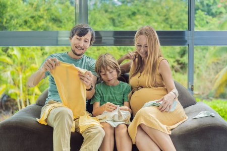 Heartwarming family moment as expectant mom, dad, and son joyfully browse through newborn babys clothes, eagerly anticipating the arrival of a new family member.