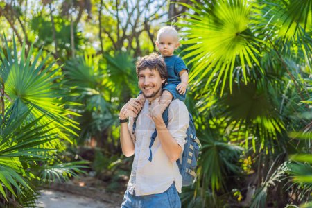 Un hombre está cargando alegremente a un bebé sobre sus hombros a través de la exuberante selva, rodeado de una variedad de plantas y vida silvestre. Ambos sonríen mientras disfrutan del paisaje natural y pasean tranquilamente.