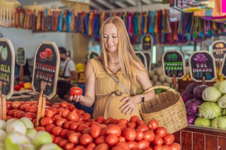 En una tienda de comestibles, una mujer embarazada está junto a un puesto de frutas, rodeada de varios alimentos naturales. Ella está en un espacio público donde el mercado local ofrece alimentos enteros para el comercio