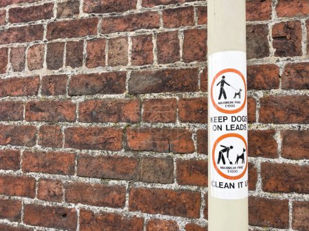 Photo for Sign on a lamppost saying keep dogs on leads and clean up dog poop beside a red brick wall - Royalty Free Image
