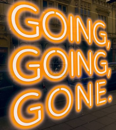Close up of a sign saying going, going, gone, in a shop window, in orange neon.