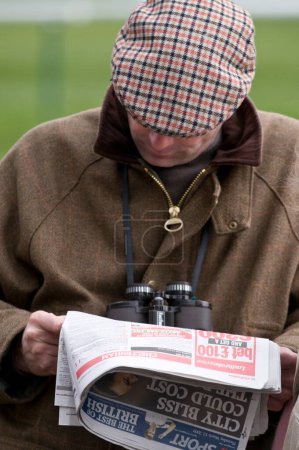 Foto de Hombre de gorra plana mirando el Racing Post listo para apostar a un caballo. Vestido para un día en las carreras - Imagen libre de derechos
