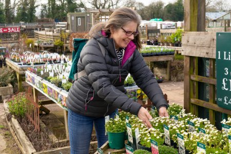 A senior woman smiling while she shops for plants at a garden centre shop on a cold day.
