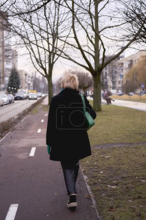              a portrait of a stylish old woman in a black coat with green accessories on a spring street                  
