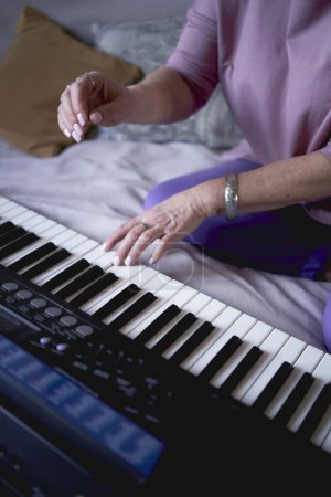 Foto de Madre de 60 años y una hija de 40 años tocan el teclado juntas en la cama en casa - Imagen libre de derechos