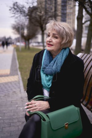              a portrait of a stylish old woman in a black coat with green accessories on a spring street                  