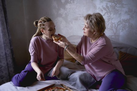 Foto de Anciana madre e hija de mediana edad comiendo pizza y viendo una película en su casa - Imagen libre de derechos
