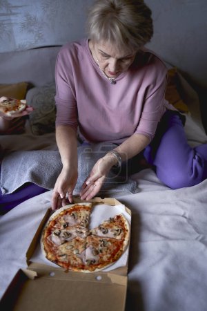 Foto de Anciana madre e hija de mediana edad comiendo pizza y viendo una película en su casa - Imagen libre de derechos