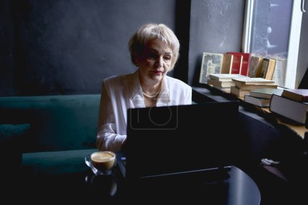 Foto de Anciana trabaja en un café en un portátil - Imagen libre de derechos