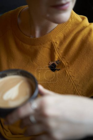    portrait of a stylish middle-aged woman in a yellow sweater with braids drinking coffee in a cafe                     