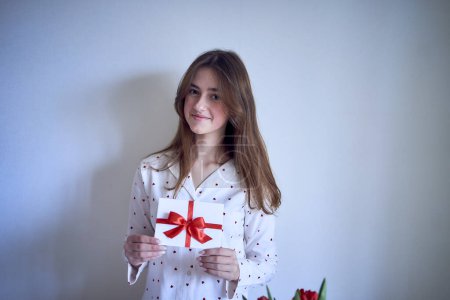 Photo for Gift certificate in the hands of a teenage girl wearing white pajamas with red hearts - Royalty Free Image