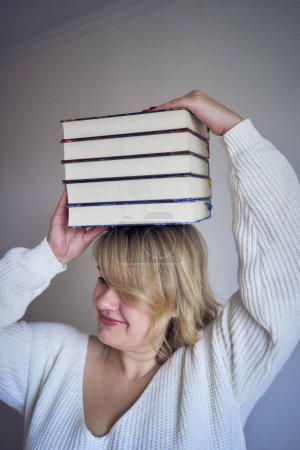medium-sized woman in light clothes plays with books in a light room