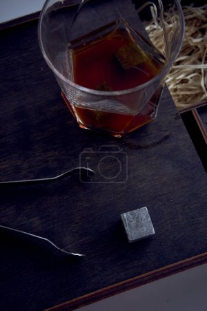 Foto de Whiskey con pinzas, cubo de piedra, caja de madera y trigo en la alfombra - Imagen libre de derechos