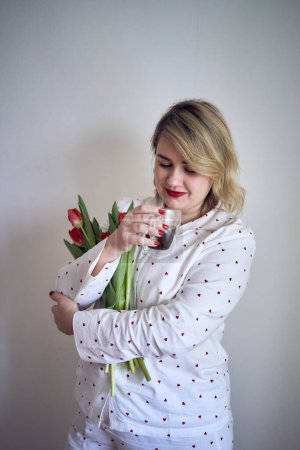          a portrait of a beautiful medium-sized woman in pajamas with a bouquet of red tulips in a minimalist style                      