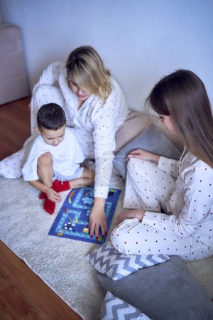           a     mother with teenage daughter and little son in pajamas playing board games on the floor                