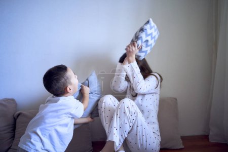 A teenage girl and her little brother are playing and hugging in a pillow fort