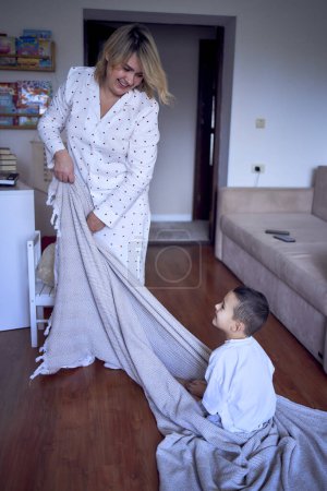 mère joue et traîne son petit fils sur un drap autour de la pièce                             