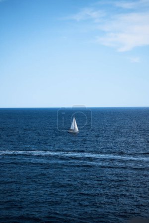        lone white sailboat surrounded by deep blue water and a clear blue sky                    