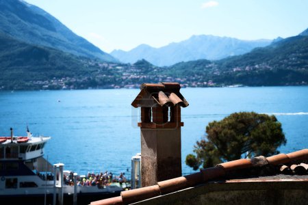           chimney on the roof in the foreground of a ferry on Lake Como                    