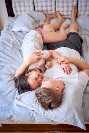 Téléchargez les photos : Jeune couple est allongé sur le lit, la fille est sur l'épaule du garçon, câlins tendres - en image libre de droit