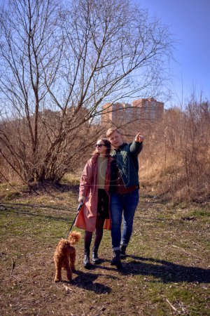 Téléchargez les photos : Élégant jeune couple marchant avec leur chien dans la nature - en image libre de droit