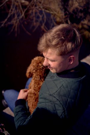 boy sits on a pier and hugs a cockapoo               